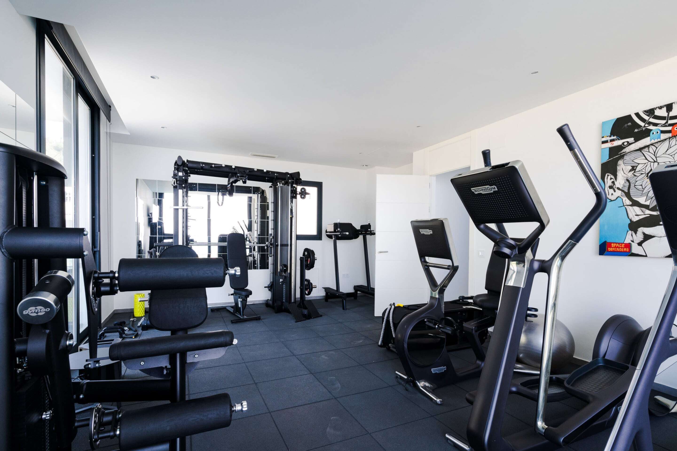 A gym with exercise equipment, a wall-mounted TV, and a large window.
