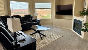 A living room with a black leather sofa, a glass coffee table, a flat-screen TV mounted on the wall, and a fireplace. - Spacious 2BR Condo with Secondary Suite on Wolf Creek Golf Course – Sleeps 8! (Mesquite)