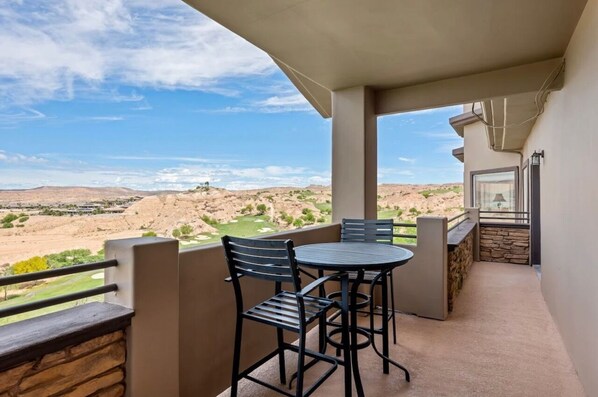 Een balkon met een tafel en stoelen, met uitzicht op een woestijnlandschap met een golfbaan.