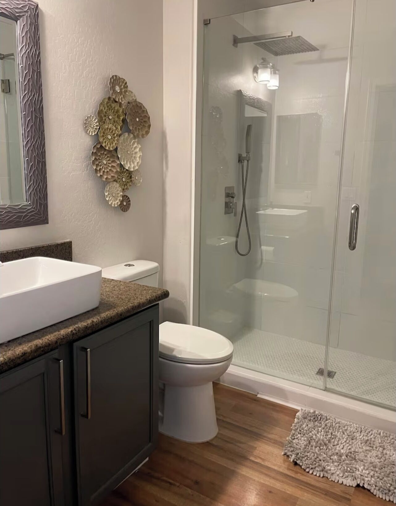Een badkamer met een wit wastafel, donkere kastjes, een toilet en een douchecabine met glazen wanden.