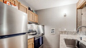 Cocina compacta con refrigerador de acero inoxidable, horno empotrado, gabinetes de madera, encimera de granito y pileta de acero inoxidable.