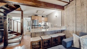 Una cocina moderna con una isla central, taburetes de madera y una escalera que sube a otro nivel.