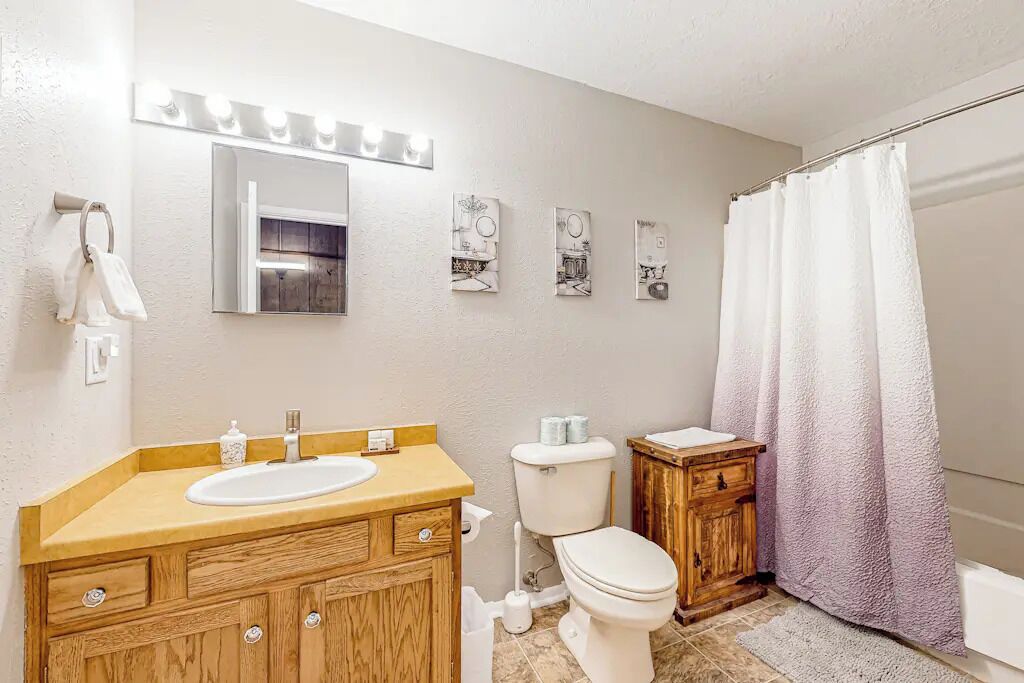 Un baño con tocador de madera, un lavabo blanco, un inodoro y una cortina de ducha.
