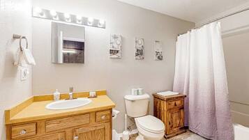 Un baño con tocador de madera, un lavabo blanco, un inodoro y una cortina de ducha.