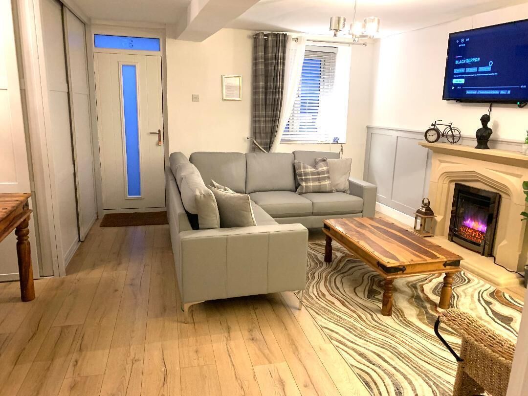 Una sala de estar con sofá, mesa de centro, chimenea y televisión montada en la pared.