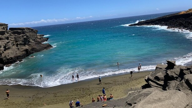 A coastal beach with rocky cliffs, clear turquoise waters, and people enjoying the beach.