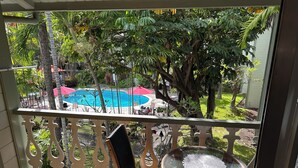 A balcony with a view of a swimming pool, surrounded by lush greenery and palm trees.
