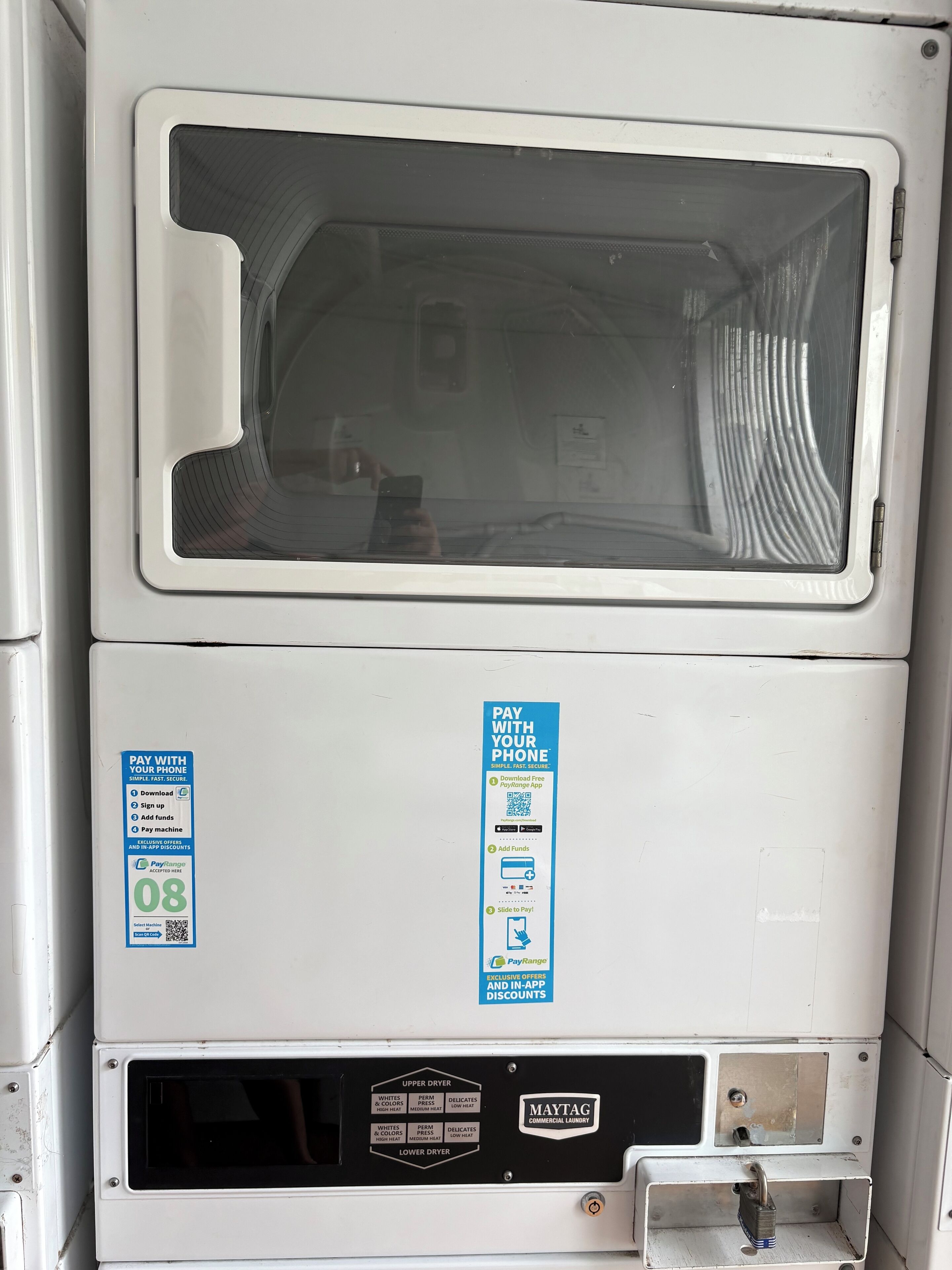 A commercial laundry machine with a large glass window, a control panel, and a payment advertisement.