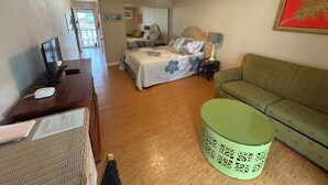A bedroom with a bed, a desk with a computer, a green chair, and a ceiling fan.