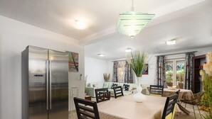Una cocina moderna con un refrigerador de acero inoxidable, un comedor con mesa y sillas, y un ventanal con cortinas.