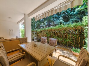 A dining area with a wooden table and wicker chairs, overlooking a lush garden with a variety of plants and trees. - Apartment in Porec Near Brijuni Islands (Porec)