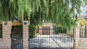 Una entrada con portón, un pilar de piedra, un cerramiento metálico y un edificio con fachada de ladrillo al fondo.
