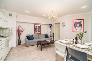 A modern living room with a grey sofa, a wooden coffee table, and a dining area set for four. - Piasek Apt - Top Location, Patio, Tram&Bus nearby - by Rentujemy (Kraków)