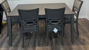 A dining area with a rectangular table and four chairs, a pendant light fixture above, and a white wall with a baseboard.
