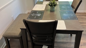 A dining table with place cards, a potted plant, and chairs in a room with wooden flooring and a view of the outdoors.