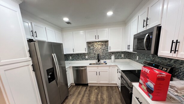 A modern kitchen with white cabinets, stainless steel appliances, and a wooden floor.