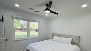 A bedroom with a bed, a ceiling fan, a window, and wooden flooring.