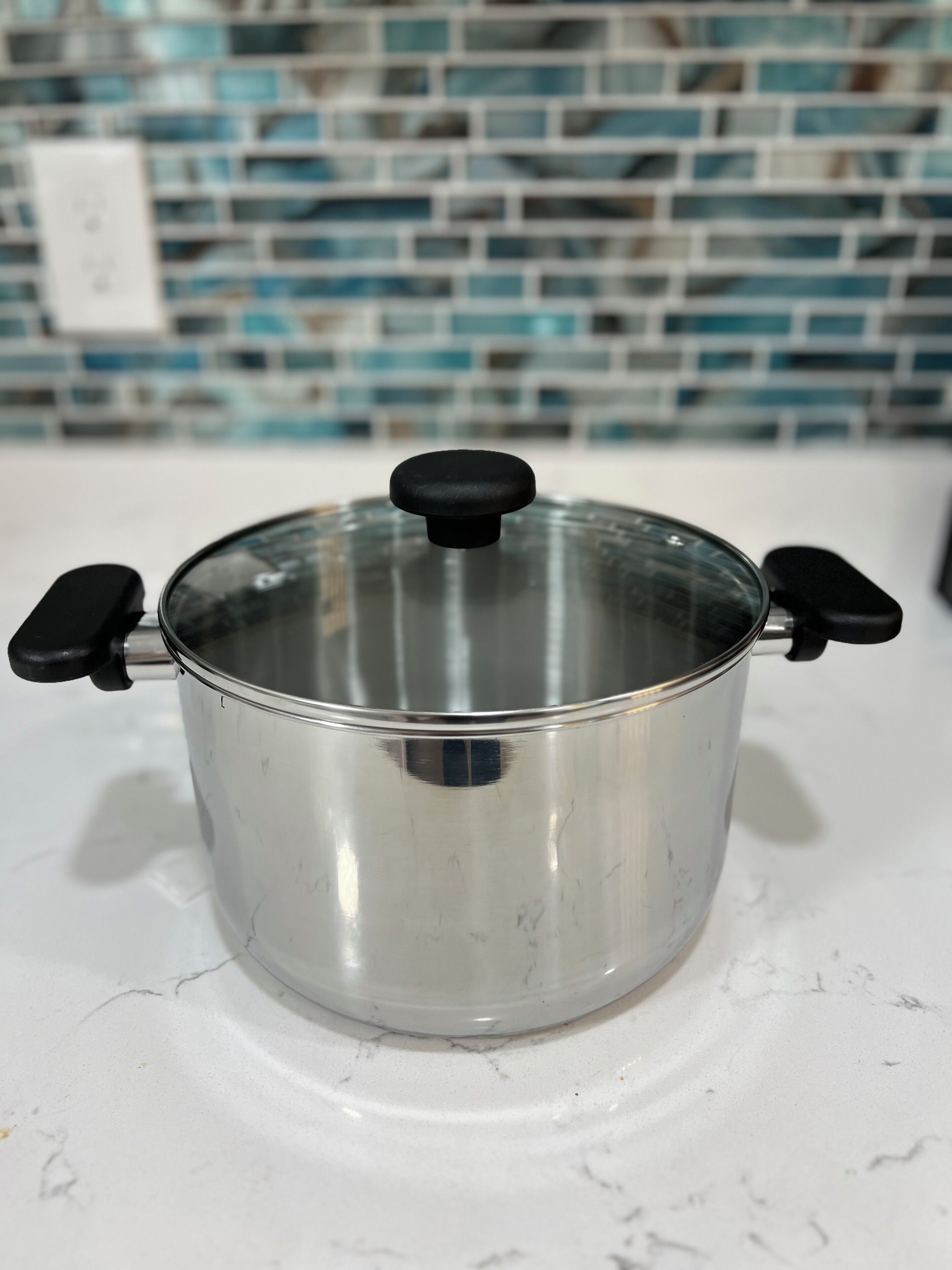 A stainless steel pot with a black knob lid on a white countertop.