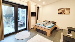Ein Schlafzimmer mit Bett, Fernseher, Fenster und Balkon.