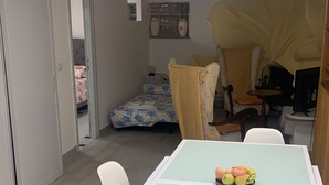 En matplats med ett bord och stolar, en säng med ett blommigt överkast och ett fönster med dekorativa föremål.