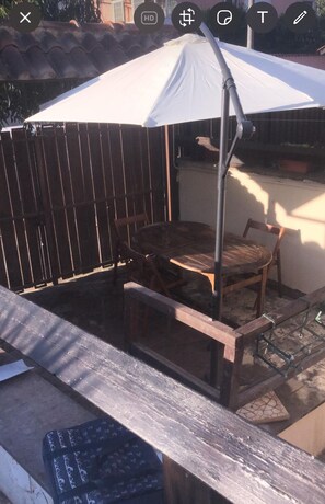 Ein Patio mit Tisch und Stühlen unter einem weißen Sonnenschirm, einem Metallgrill und einem Holzzaun.