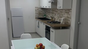 Ett modernt kök med vita skåp, ett matbord med glasskiva och en fruktskål.