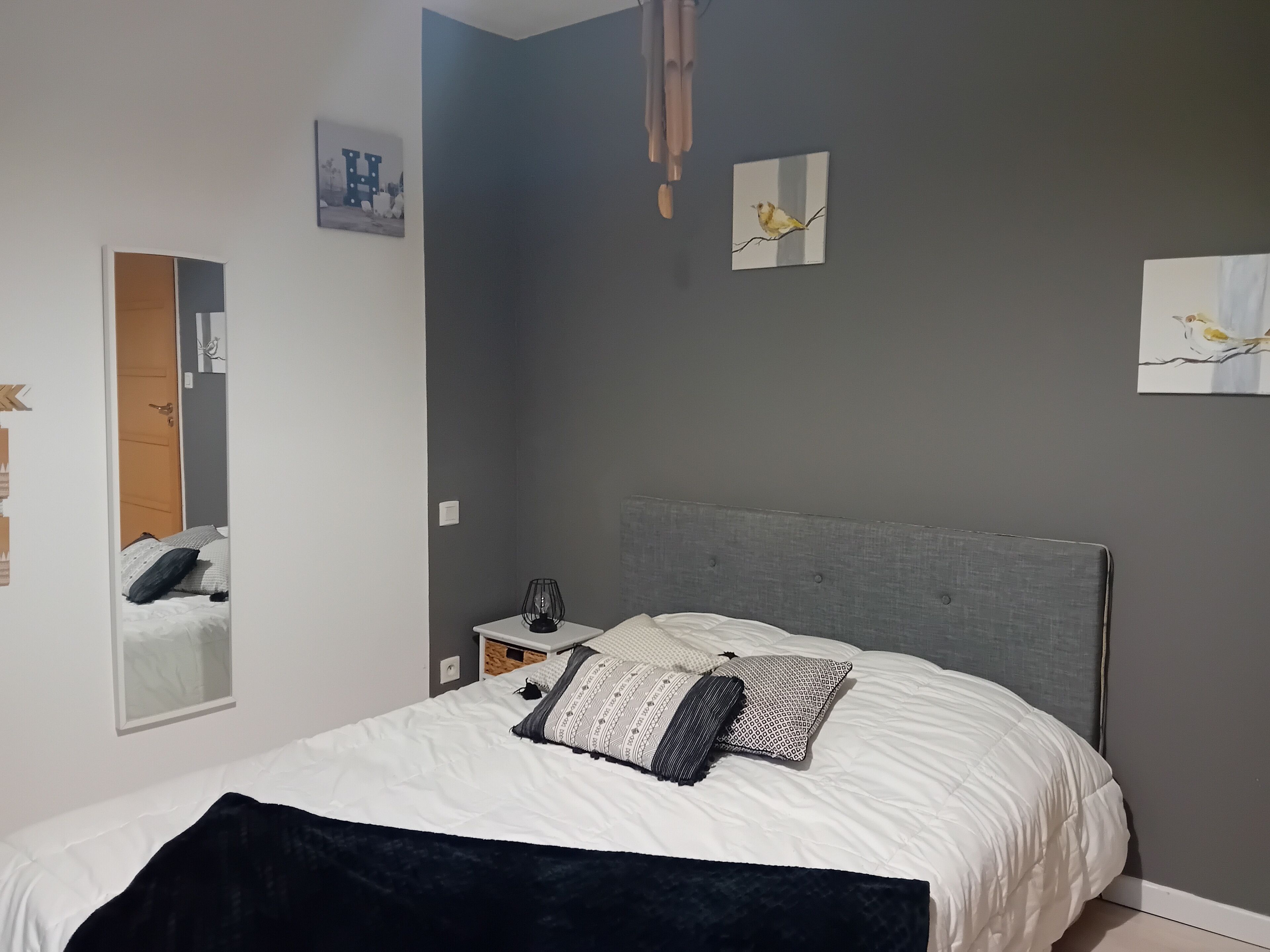 A bedroom with a bed, a nightstand, a mirror, and wall art.