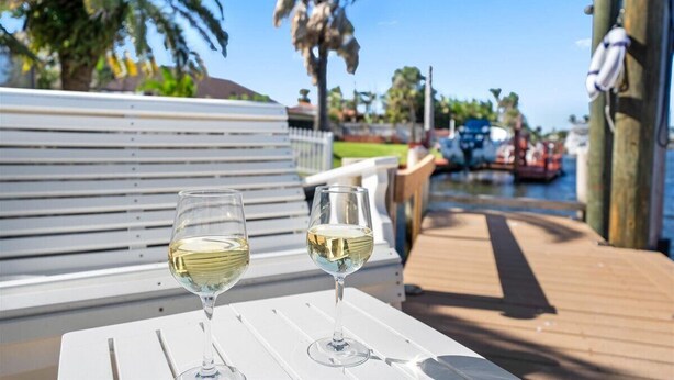 Twee glazen witte wijn op een witte tafel met een houten terras en uitzicht op een jachthaven met boten.