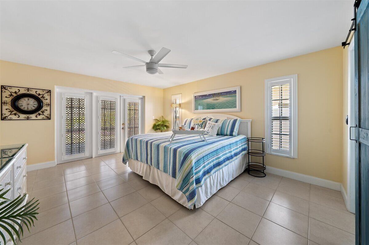 A bedroom with a bed, a ceiling fan, a clock, and a window with blinds.