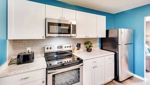 Una cocina moderna con gabinetes blancos, un refrigerador de acero inoxidable, un microondas y una estufa.