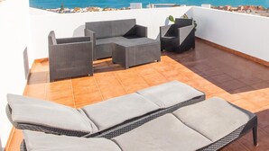 A rooftop terrace with a view of the sea, featuring wicker furniture and a sun lounger.