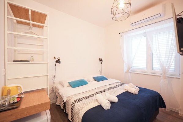 Un dormitorio con cama, mesitas de noche, armario y ventana con cortinas.