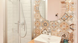 A bathroom with a glass-enclosed shower, a wooden vanity with a white sink, and a tiled wall with a geometric pattern. - Zaratino rooms (Zadar)