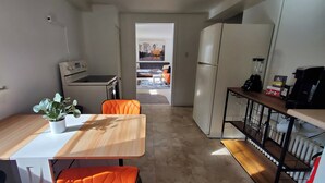Una cuina compacta amb zona de menjador, nevera, cafetera i taula petita amb una planta en test.
