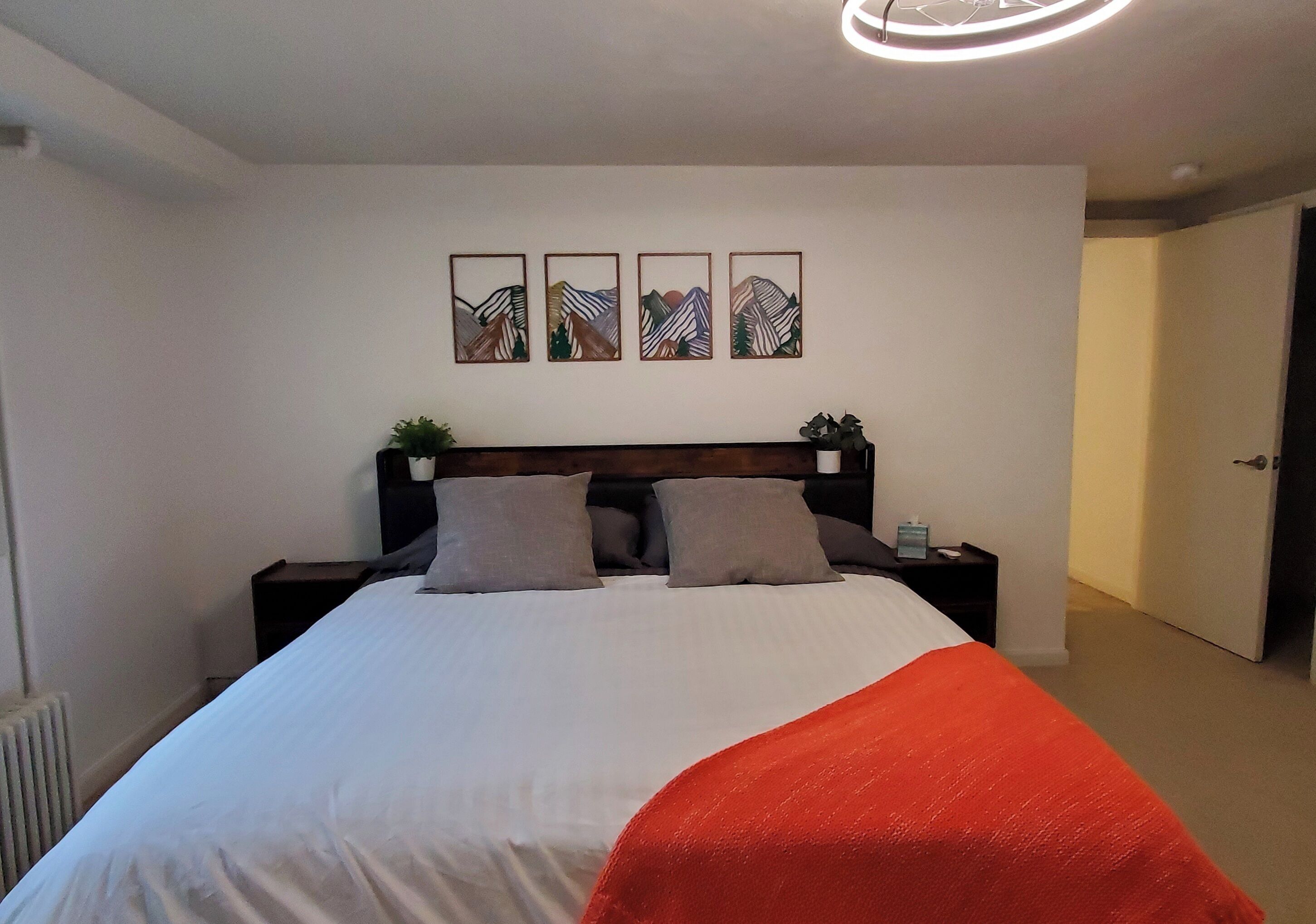 A neatly made bed with a white and red blanket, a wooden headboard, and three framed artworks on the wall above.