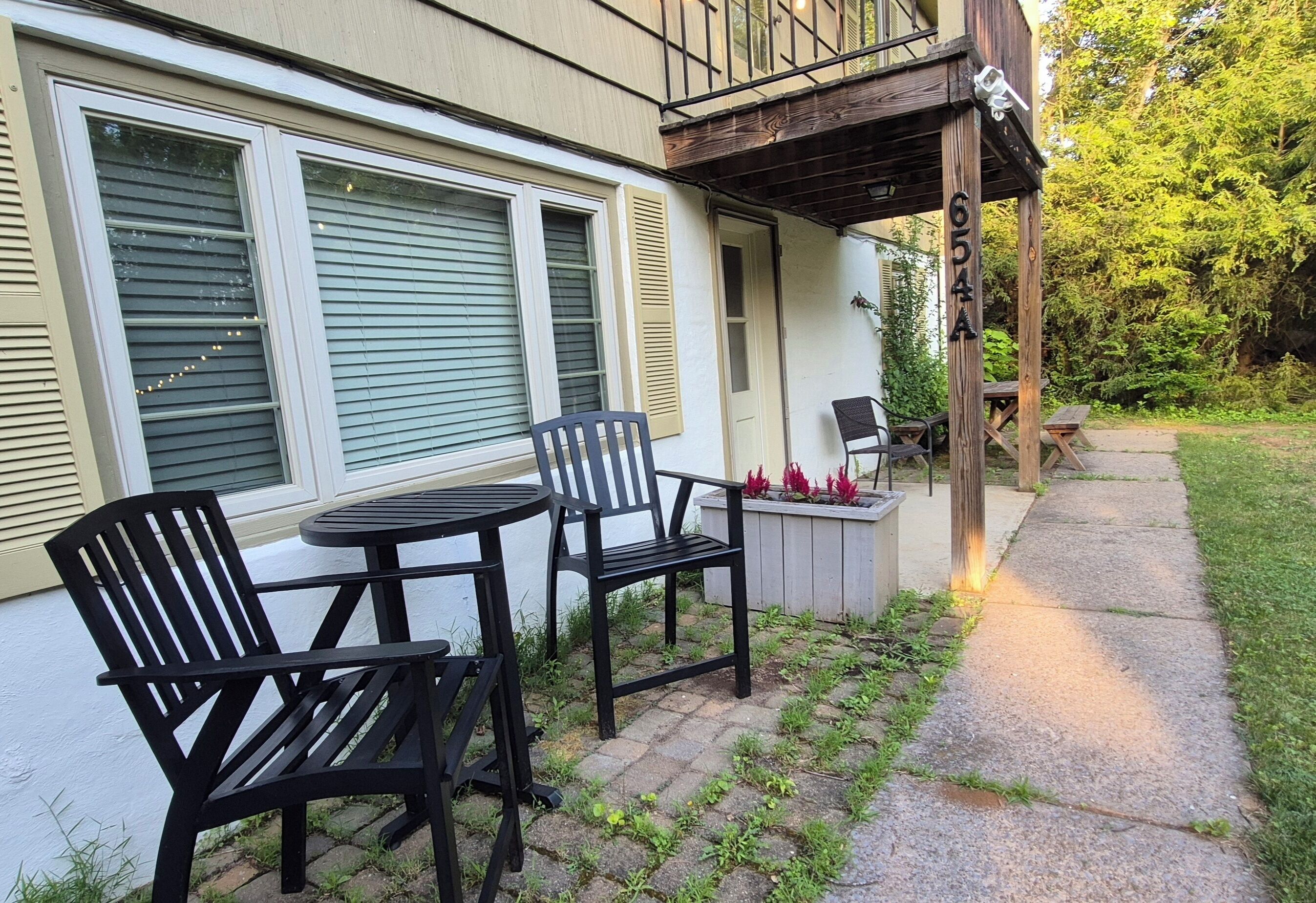 Een terras met twee zwarte stoelen en een kleine tafel, een houten terras en een wit gebouw met luiken.