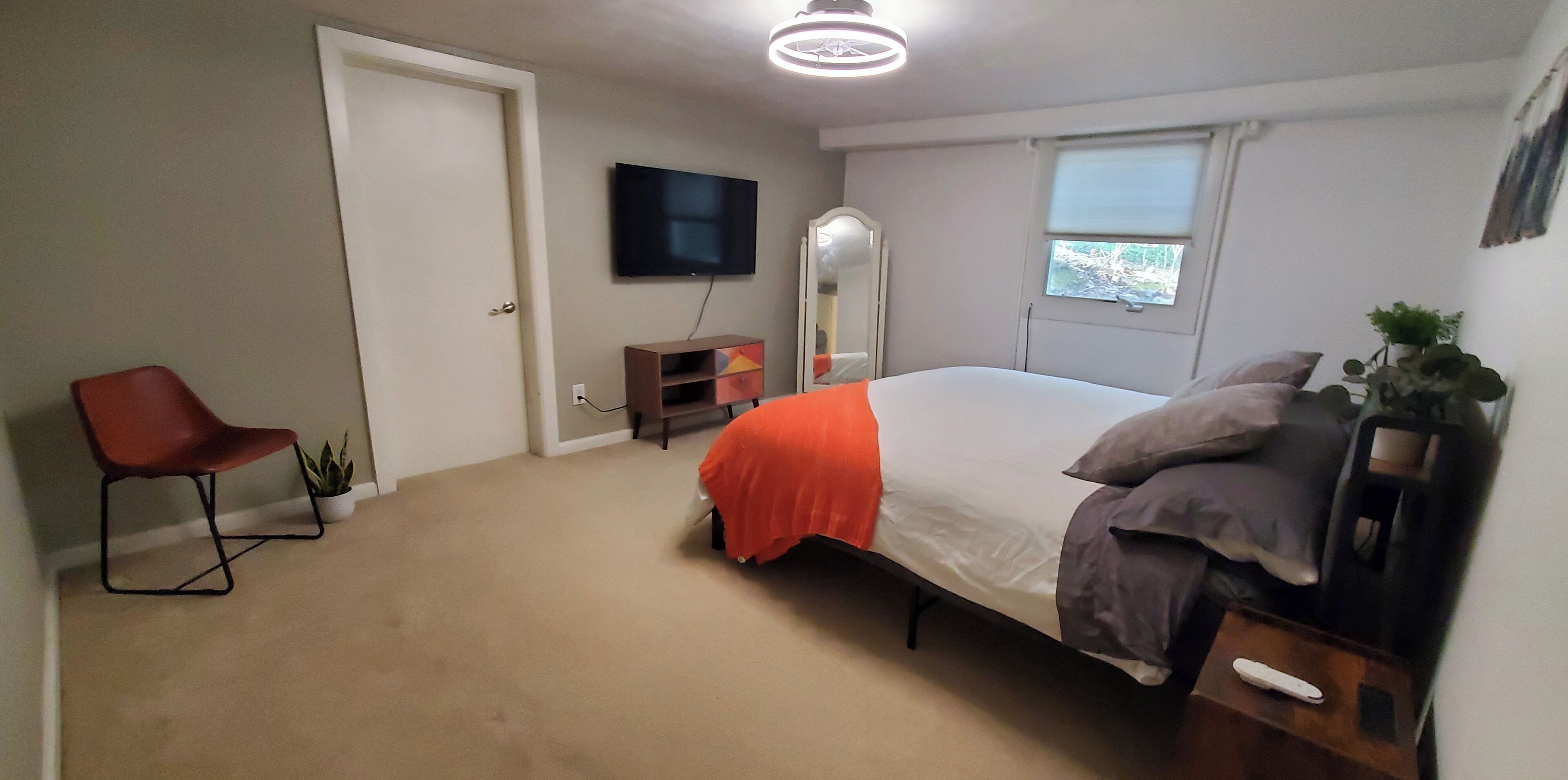 A bedroom with a bed, a chair, a TV, a mirror, and a window.