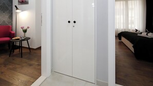 A modern hotel room with a white wardrobe, a bed with a black headboard, a small table with a vase of flowers, and a red armchair. - Zadar Luxury Rooms (Zadar)