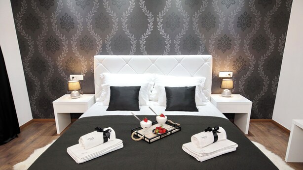 A neatly made bed with a dark bedspread, two white pillows, and a tray with towels and a small dessert. - Zadar Luxury Rooms (Zadar)