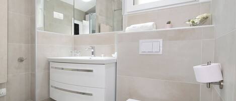 A modern bathroom with a white vanity, a toilet, and a large mirror.