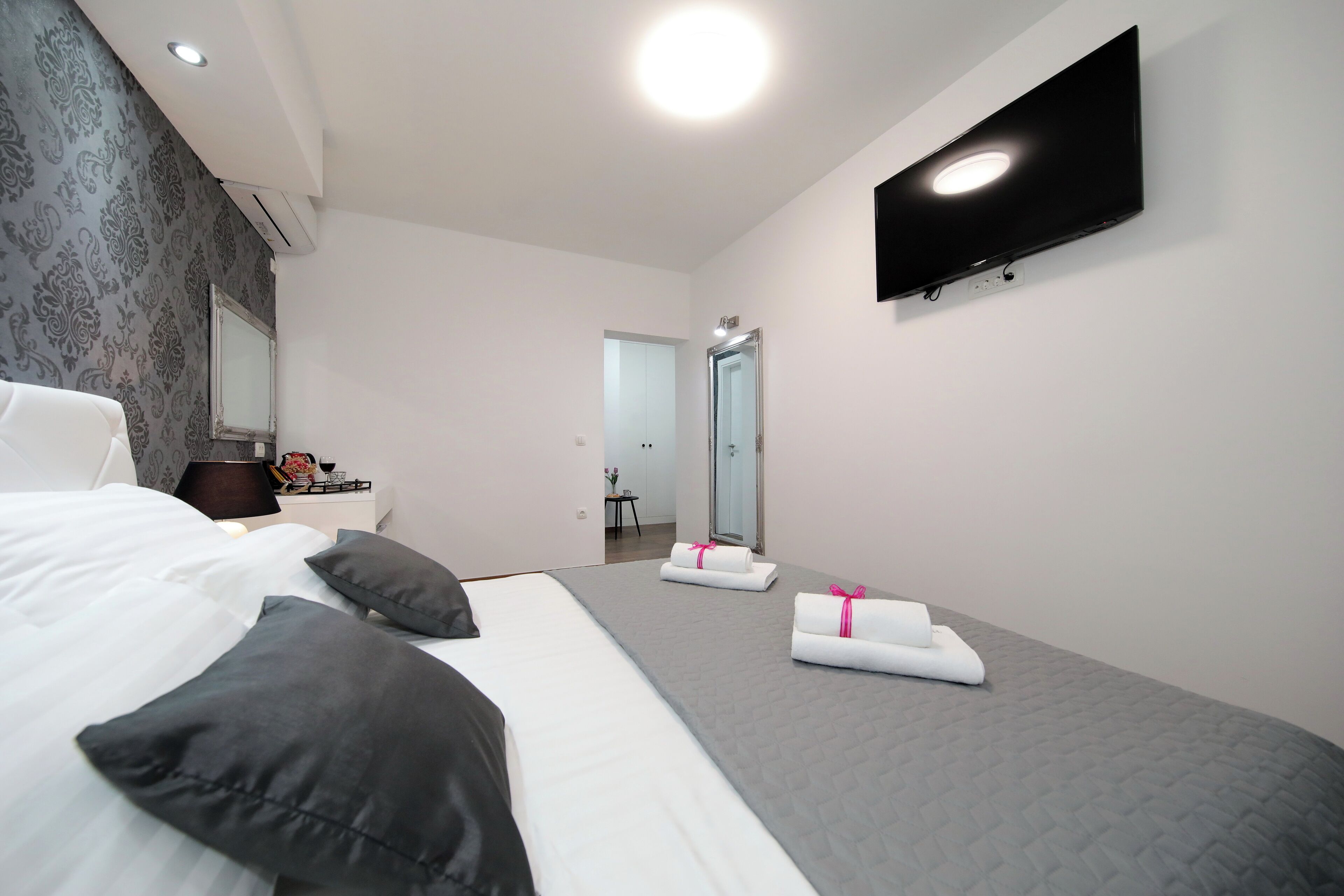 Una habitación de hotel moderna con una cama grande, un televisor de pantalla plana montado en la pared y un pequeño escritorio con una lámpara.