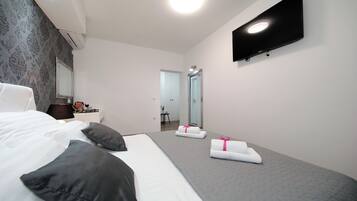 Una habitación de hotel moderna con una cama grande, un televisor de pantalla plana montado en la pared y un pequeño escritorio con una lámpara.