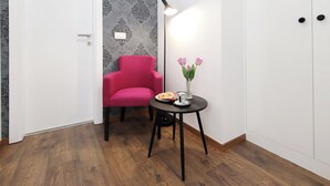 A room with a wooden floor, a white door, a red chair, a small table with a vase of flowers, and a white wardrobe. - Zadar Luxury Rooms (Zadar)