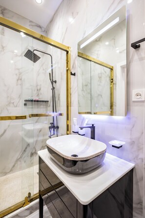 A modern bathroom with a glass-enclosed shower, a marble vanity, and a large mirror. - Amir Temur avenu 123  (Tashkent)