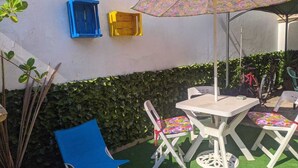 An outdoor patio with a table and chairs, a blue chair, a yellow and blue cabinet, and a patterned umbrella.