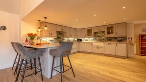 A modern kitchen with a central island, bar stools, and a wooden floor.