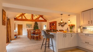 A spacious kitchen with a central island, wooden beams on the ceiling, and a dining area with a Christmas tree.