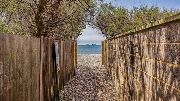 A pathway leading to a beach with wooden fences on either side.