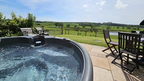 A hot tub on a patio with chairs and a view of a vineyard.