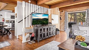 A modern living room with a large flat-screen TV, wooden beams, a dining area with a table and chairs, and a cozy seating area with a sofa and patterned cushions. - Guest FAV Luxury Sun Chalet + Hot Tub + BBQ (Big Bear Lake)